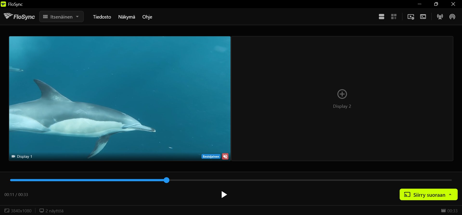 FloSyncin ohjauspaneeli, jossa Display 1:llä on delfiinivideo, tyhjä Display 2 näyttää plus-merkin, aikajana on edennyt osittain, ja alapalkissa on toisto- ja Siirry suoraan -painikkeet.