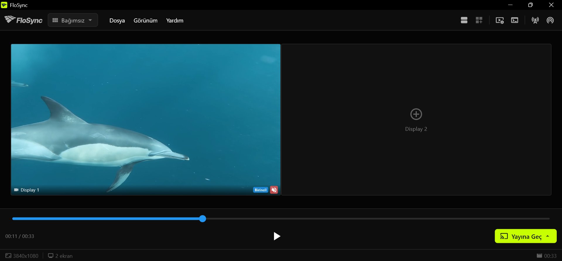 FloSync'in kontrol paneli; Display 1'de bir yunus videosu, artı işareti gösteren boş bir Display 2, kısmen ilerlemiş zaman çizelgesi, alt çubukta oynat ve Yayına Geç düğmeleri.
